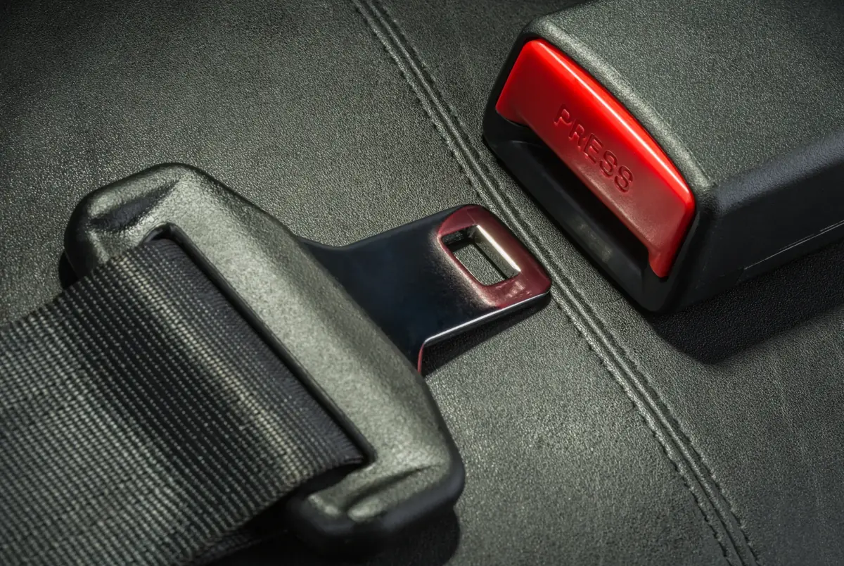 Seat belt latch tongue lying beside an open buckle with a red press release on a dark leather seat