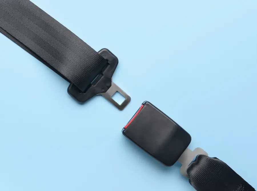 Seat belt webbing with latch tongue on one side and matching buckle on the other, laid out on a pale blue surface