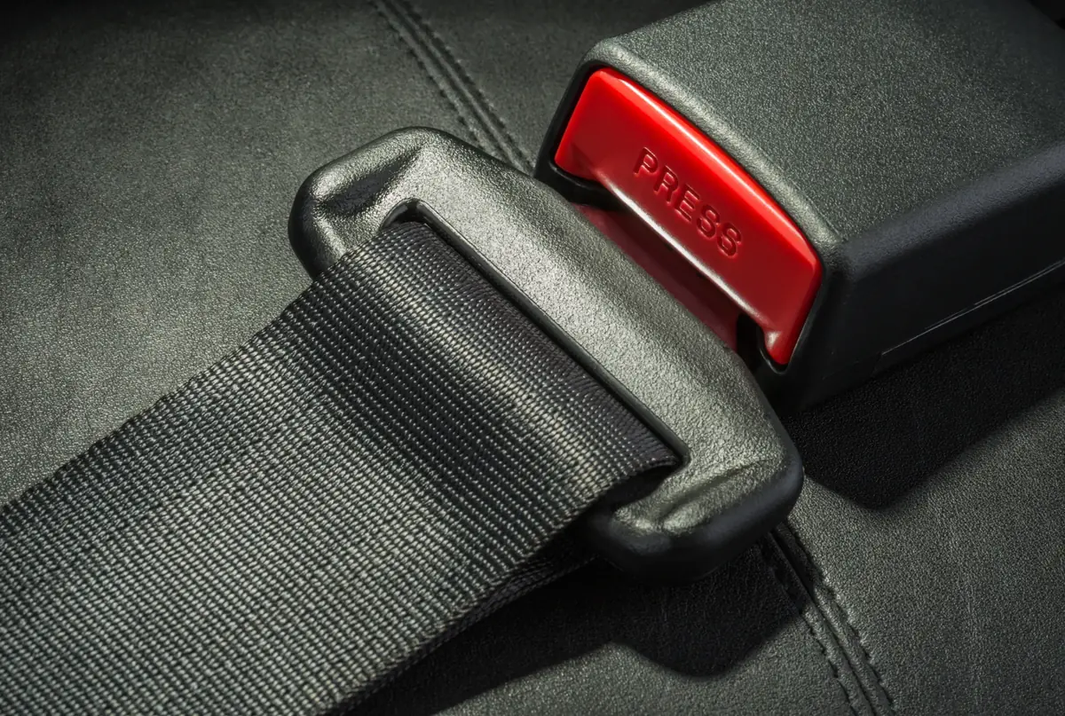 Close-up of seat belt webbing held by a latch tongue seated in a buckle with a red press release