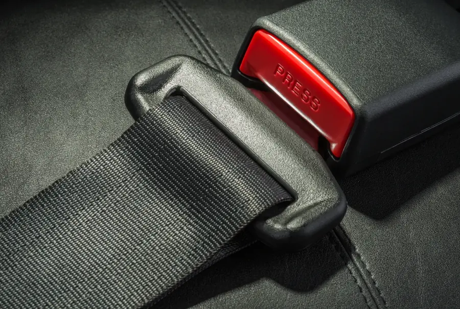 Close-up of seat belt webbing held by a latch tongue seated in a buckle with a red press release