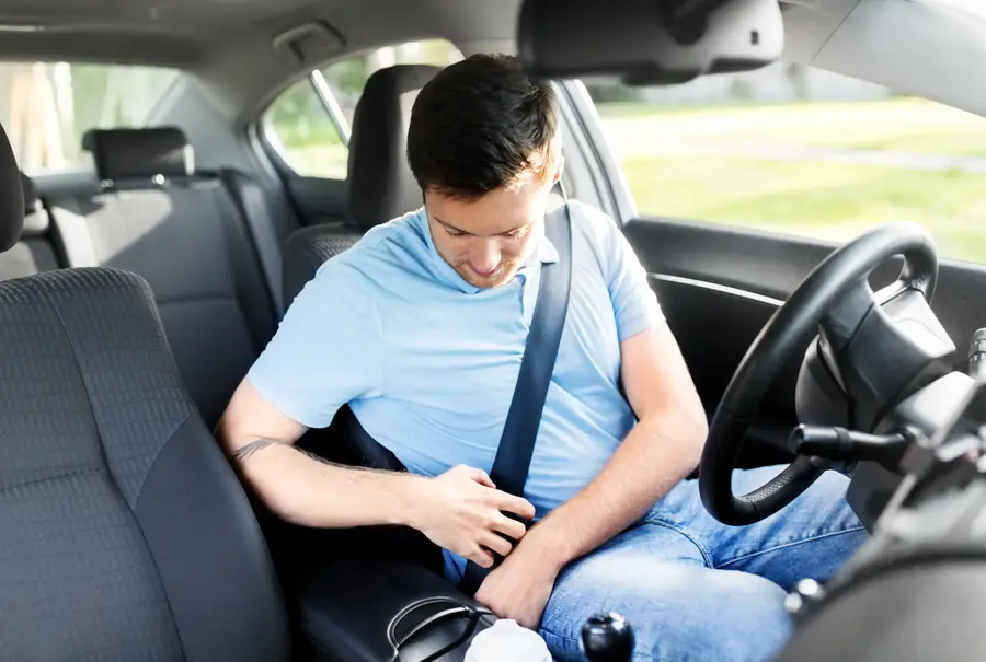 Driver in a blue shirt fastening a seat belt in a car with a wide view of the cabin interior