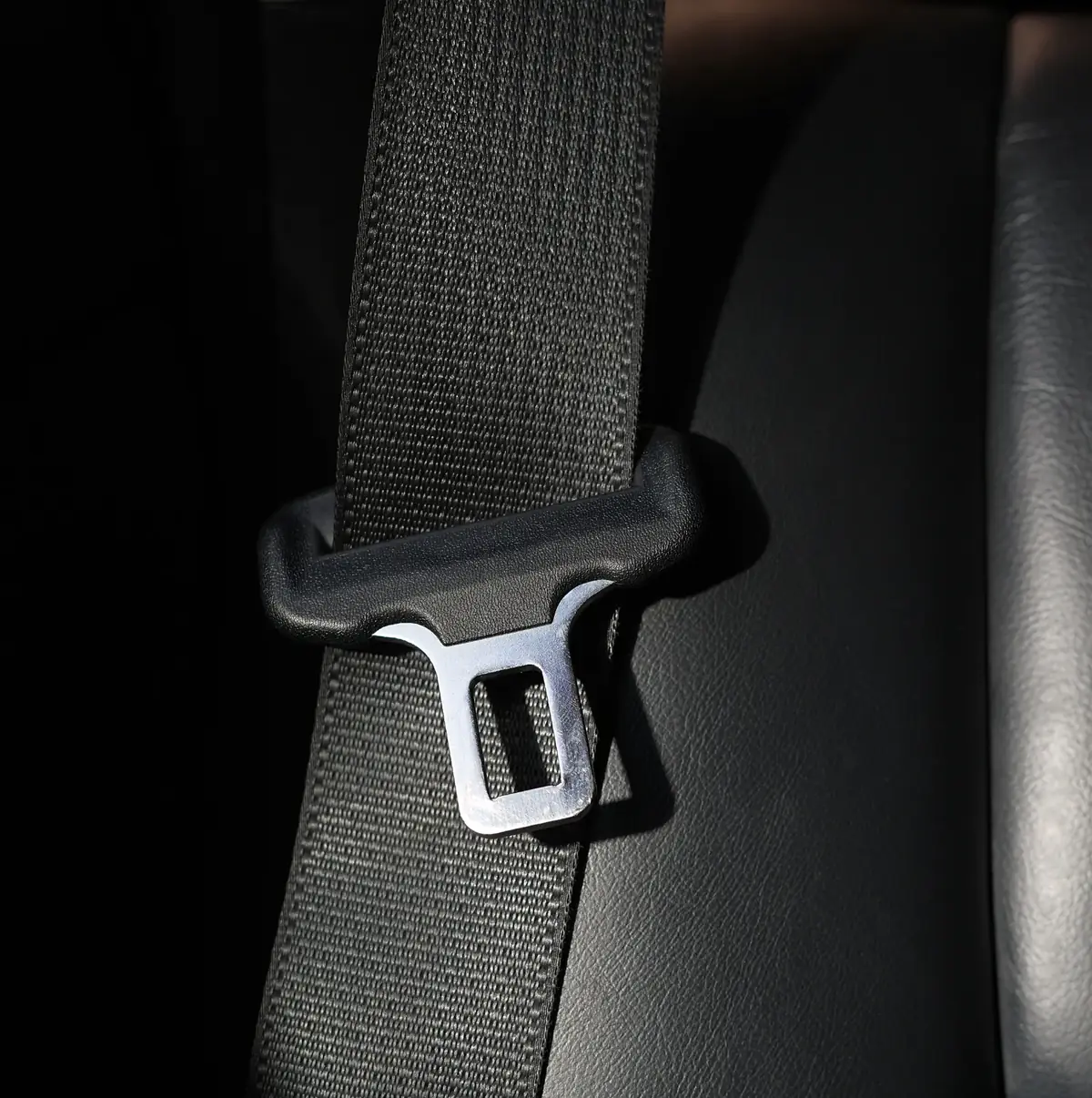Seat belt webbing passing through a moulded pillar loop with the metal latch plate resting against a dark vehicle interior