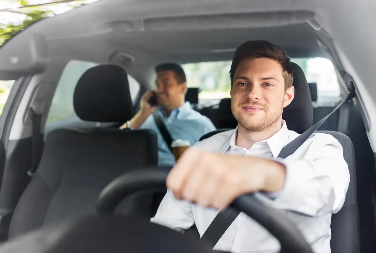 Belted driver at the wheel of a commercial passenger vehicle with a belted passenger seated behind