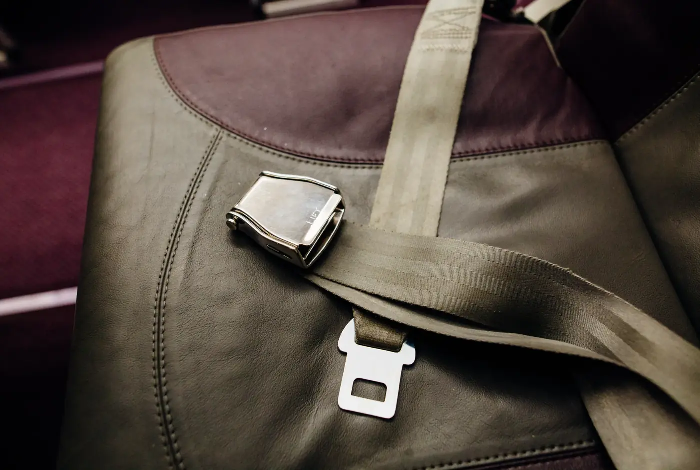 Polished metal lift-latch seat belt buckle with webbing lying across a leather passenger seat