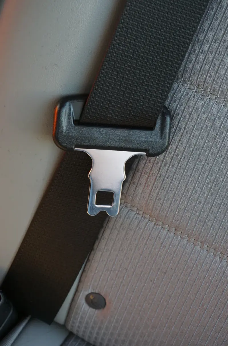 Chrome seat belt latch plate seated in a black moulded pillar loop, viewed closely against grey trim