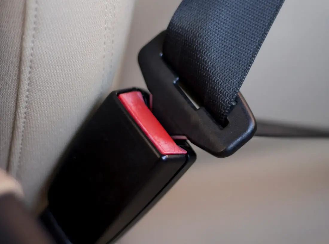 Black seat belt buckle with a red release button positioned beside a latch tongue in a pillar loop